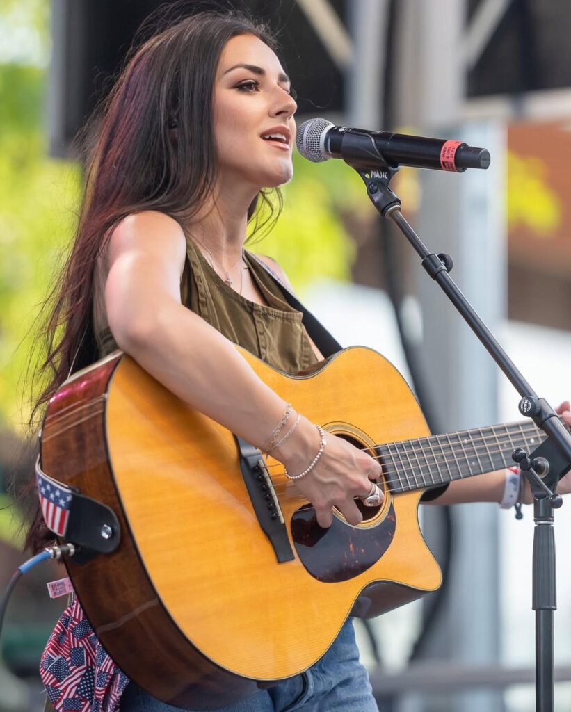 Alexis Wilkins singing onstage with a guitar